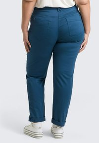 Blauwe taps toelopende broek met een hoge taille, opgerolde pijpen en achterzakken, gecombineerd met witte sneakers en enkelsokken.
