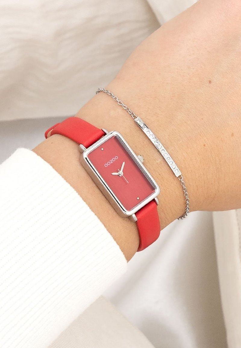 Montre analogique rectangulaire rouge avec des éléments en métal argenté ; dotée d'un cadran rouge, de cadrans minimaux et d'un bracelet en silicone rouge. Accompagnée d'un bracelet en argent.