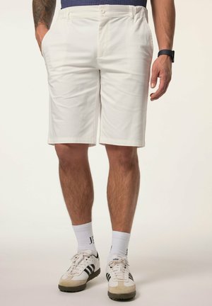 Mężczyzna noszący białe szorty do kolan, białe buty Adidas z czarnymi paskami, białe skarpety sportowe i czarny zegarek na rękę.