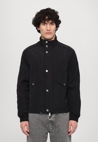 Black jacket made of smooth fabric, featuring a high collar, snap buttons, and two front pockets. Simple design with a relaxed fit.