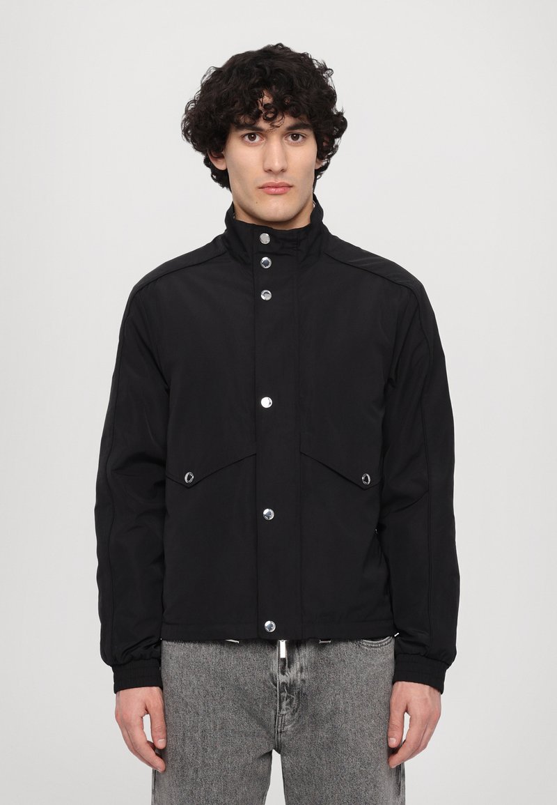 Black jacket made of smooth fabric, featuring a high collar, snap buttons, and two front pockets. Simple design with a relaxed fit.