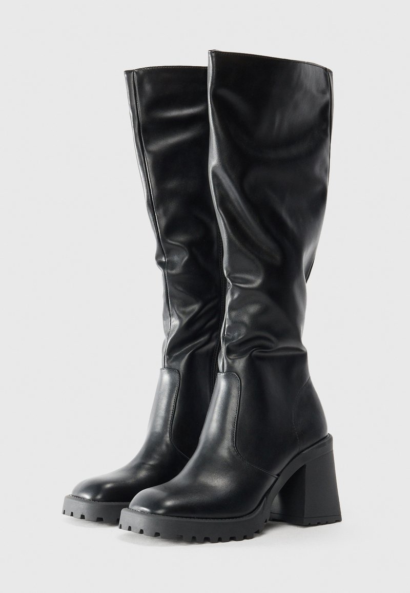 Bottes en cuir noir montantes, avec un bout rond, un talon épais et une semelle texturée. Présente des plis doux dans le matériau.