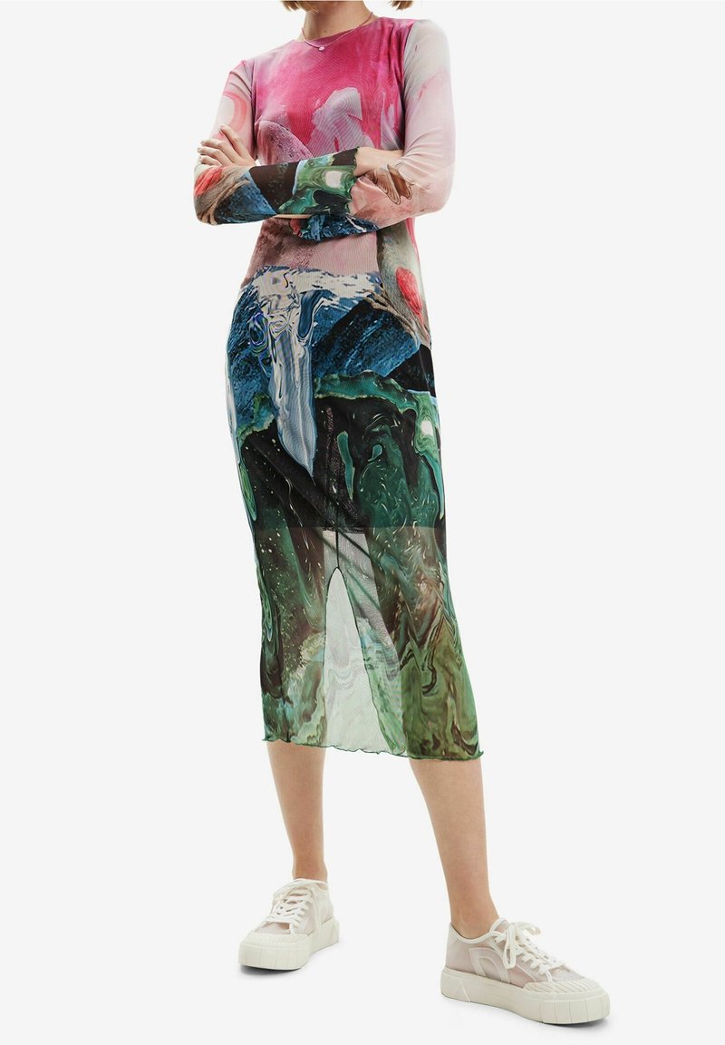 Robe à manches longues en tissu transparent avec un imprimé abstrait coloré, comprenant des nuances de rose, vert et bleu, associée à des baskets blanches.
