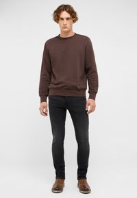 Brązowa bluza z bawełnianej mieszanki, z okrągłym dekoltem, z prążkowanymi mankietami i dołem. Noszona z ciemnymi dżinsami i brązowymi skórzanymi butami.