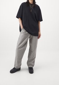 Černé oversized tričko, šedé kalhoty s viditelným švem a černé tenisky. Jednoduchý, volný design s neutrálními barvami.