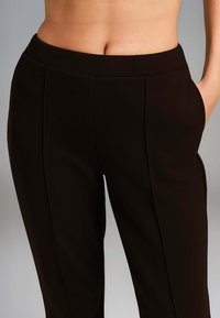 Pantaloni neri su misura con una texture liscia, caratterizzati da una vita alta, tasca sul fianco e dettagli delle cuciture delicati lungo la parte anteriore.