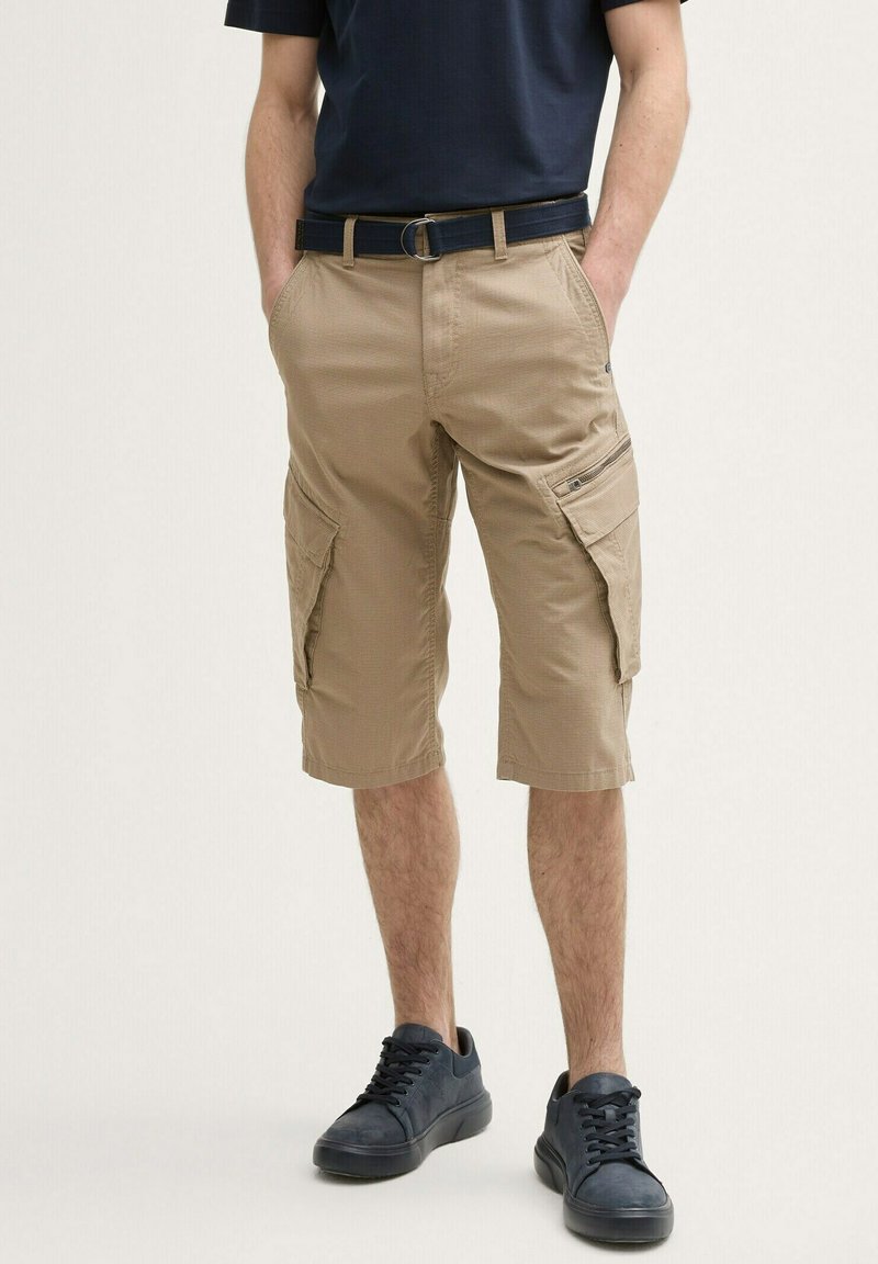 Beige cargo shorts med sidelommer, lavet af struktureret stof. Sammen med en marineblå t-shirt og mørke sneakers, med et bælte.