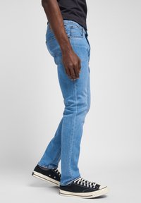 Jasnoniebieskie dżinsy o slim fit, z widocznymi szwami, kieszeniami bocznymi i przetartym dołem, w połączeniu z czarnymi sneakersami.