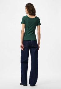 Top curto verde canelado com decote largo em forma de U, combinado com jeans escuros de corte solto, exibindo um design casual e descontraído.