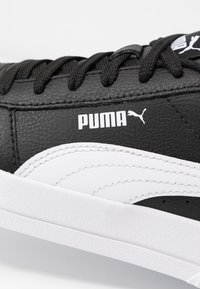 Svarta lädersneakers med vitt accent på sidan, med en texturerad finish, svarta snören och en framträdande vit Puma-logotyp.