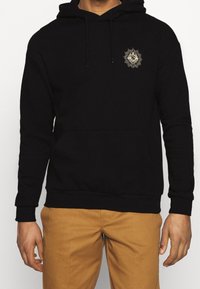 Sweat à capuche noir en mélange de coton, avec une poche kangourou à l'avant, des cordons de serrage, et un motif graphique doré sur le côté gauche de la poitrine.