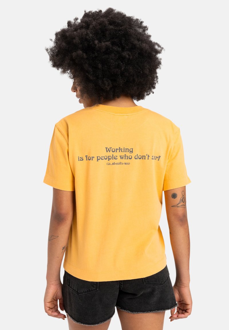 Yellow cotton T-shirt with short sleeves and a rounded neckline. The back features black printed text: "Working is for people who don’t surf."