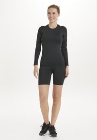 Zwarte sportieve longsleeve top gecombineerd met zwarte compressiekorte broek, met een soepele stof en een fitted ontwerp. Draag het met zwarte sportschoenen.