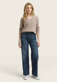 Beige knitted sweater with a v-neck and ribbed texture paired with wide-leg dark blue jeans and white sneakers.