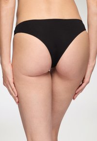 Culotte bikini in cotone nero con un design a gamba alta, texture liscia e dettagli di cucitura minimi. L'elastico in vita si posiziona basso sui fianchi.