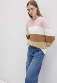 Strickpullover mit pinken, weißen, beigen und braunen Streifen. Lockerer Schnitt mit weit geschnittenem Ausschnitt, kombiniert mit hellblauen Jeans.