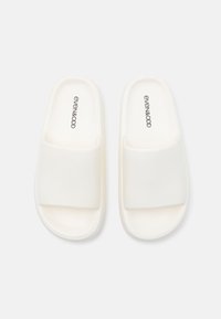 White slide sandals with a textured fabric strap and smooth rubber sole. Features subtle branding on the insole. Simple, minimalist design.