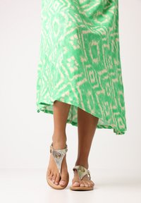 Groene tie-dye maxi jurk met een high-low zoom en een paar zilverkleurige sandalen met decoratieve hardware en een gestructureerd ontwerp.