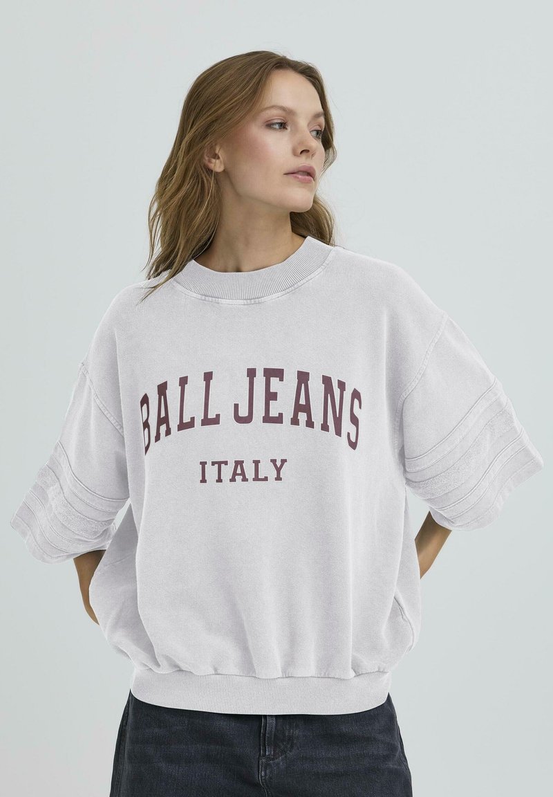 Sweatshirt oversized de culoare gri deschis, cu mâneci scurte, având inscripția "BALL JEANS ITALY" în text burgund. Textură netedă și guler rib poziționat.