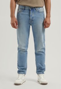 Jeans de mezclilla azul claro con un corte relajado, con cierre de botón y cinco bolsillos, combinados con zapatillas blancas.