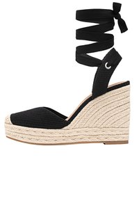 Sandale à plateforme compensée en espadrille noire avec une plateforme en jute tressé et une sangle qui s'enroule autour de la cheville.