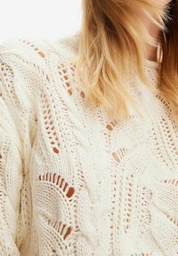 Sweter w sploty w kolorze off-white z teksturowanym wzorem, z detalami ażurowymi i luźnym krojem. Miękki, gruby materiał.