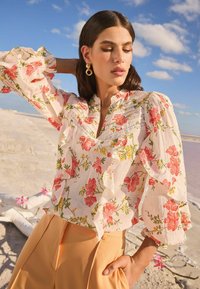 Blusa con motivo floreale in tessuto leggero, caratterizzata da maniche arricciate, scollo a placket e colori pastello con fiori rosa e gialli.