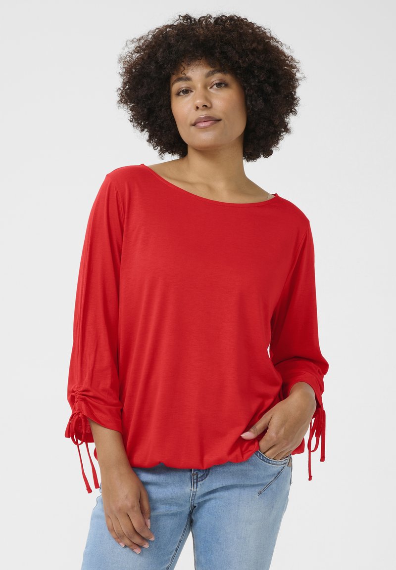 Red long-sleeve shirt with a boat neckline and gathered sleeves featuring ties. Soft, lightweight fabric, styled with a relaxed fit.