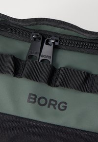 Black zippered bag with green interior, featuring a logo, durable synthetic material, and horizontal webbing detail near the zipper.
