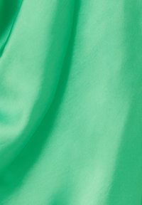 Tissu vert vif avec une texture lisse et brillante, drapé et froissé, montrant de la profondeur et un éclat subtil. Aucun motif ni élément matériel visible.