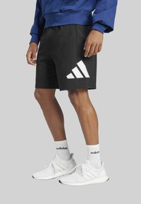 Black athletic shorts with white three-striped design on the side, paired with white sneakers and ankle-length socks with black branding.
