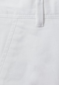 Nahaufnahme von weißem Denimstoff mit sichtbaren Nähten und einer Gürtelschlaufe.