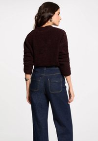 Maglione fuzzy di un borgogna scuro con scollatura a girocollo, abbinato a jeans a vita alta blu scuro a gamba larga con tasche posteriori e cuciture a contrasto.