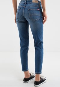 Kitsad sinised denim teksapüksid keskmise kõrguse vöökohtadega, narmastega äär ja tagataskud. Kombineeritud mustade kanvas tennisetega, millel on valged paelad.