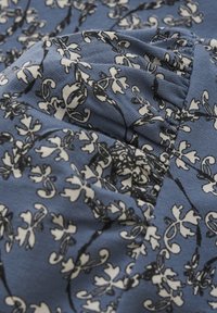 Blauer Stoff mit schwarz-weißen Blumenmustern, einer strukturierten Oberfläche, gerafften Details und sanftem Fall.