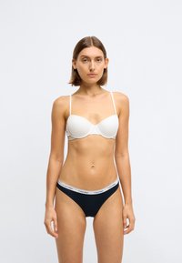 Bílý podprsenkový korzet s tenkými ramínky a hladkým materiálem. �Černé bikinové kalhotky s bílým pruhem s logem Calvin Klein. Jednoduchý, přiléhavý design.