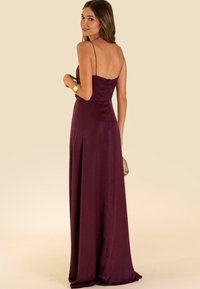Abito da sera in satin bordeaux con spalline sottili, un corpino aderente e una gonna fluente che scende fino al pavimento. La schiena presenta una chiusura con cerniera.