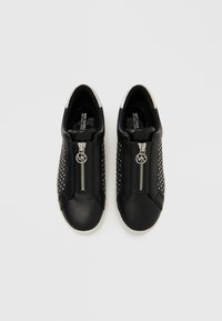 Czarne trampki z gładką skórzaną cholewką, srebrnym zamkiem błyskawicznym i perforowanym wzorem. Biała gumowa podeszwa i widoczne akcenty z logo.