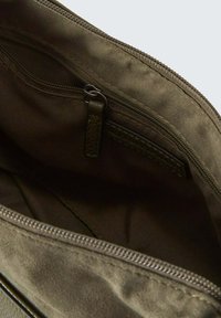 Innenraum einer olivgrünen Stofftasche mit einer Reißverschlusstasche, glatter Textur und Stichdetails an den Nähten. Reißverschlussverschluss für sicheren Zugang.