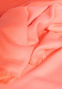 Sciarpa rosa corallo realizzata in tessuto morbido e leggero, con una superficie liscia e bordi frangiati, piegata e parzialmente drappeggiata.