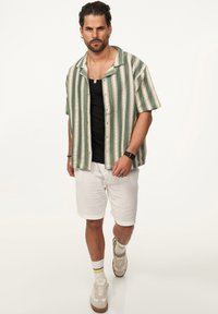 Kurzärmliges grün- und cremeweiß gestreiftes Shirt, schwarzes Tanktop, weiße strukturierte Shorts, beigefarbene Sneaker und mehrfarbige gestreifte Socken.