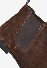 Ruskean mokkanahkasaappaat, joissa on elastiset sivupaneelit, pyöreä kärki ja sileä musta pohja. Teksturoitu päällinen, jossa on ompelut yksityiskohdat.