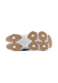 Såle av en hvit New Balance-sneaker med beige gummitrekkere og diamantformede gule innsatser.