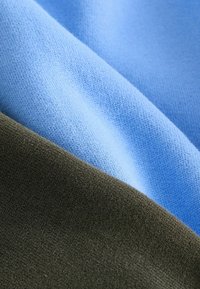 Tissu tricoté doux en deux couleurs—bleu clair et vert olive—plié avec une texture visible et des détails de couture fins.