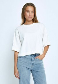 Camiseta blanca corta con cuello redondo y mangas cortas, combinada con jeans de talle alto de color azul claro. Textura de algodón suave.