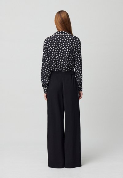 Blusa nera floreale con design a colletto, abbinata a pantaloni neri a vita alta e gamba larga. La blusa presenta piccoli fiori bianchi.