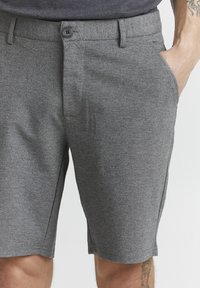 Shorts en mélange de coton gris avec une coupe structurée, fermeture à bouton et poches latérales. La surface présente un motif texturé subtil.
