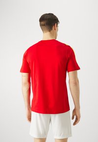 Rode katoenen t-shirt met korte mouwen, met gele accenten op de schouders. Het ontwerp is eenvoudig met een klassieke ronde hals.