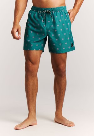 Shorts de bain verts avec un motif de palmiers violets, taille élastique avec cordon de serrage et écusson logo sur le côté.