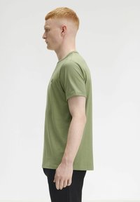 T-shirt in cotone verde oliva con collo rotondo, maniche corte e un piccolo logo ricamato sul petto. Texture liscia, vestibilità regolare.